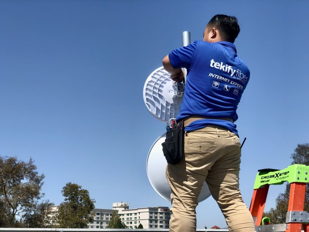 Tekify technician installing a fiber-fed wireless dish on a rooftop